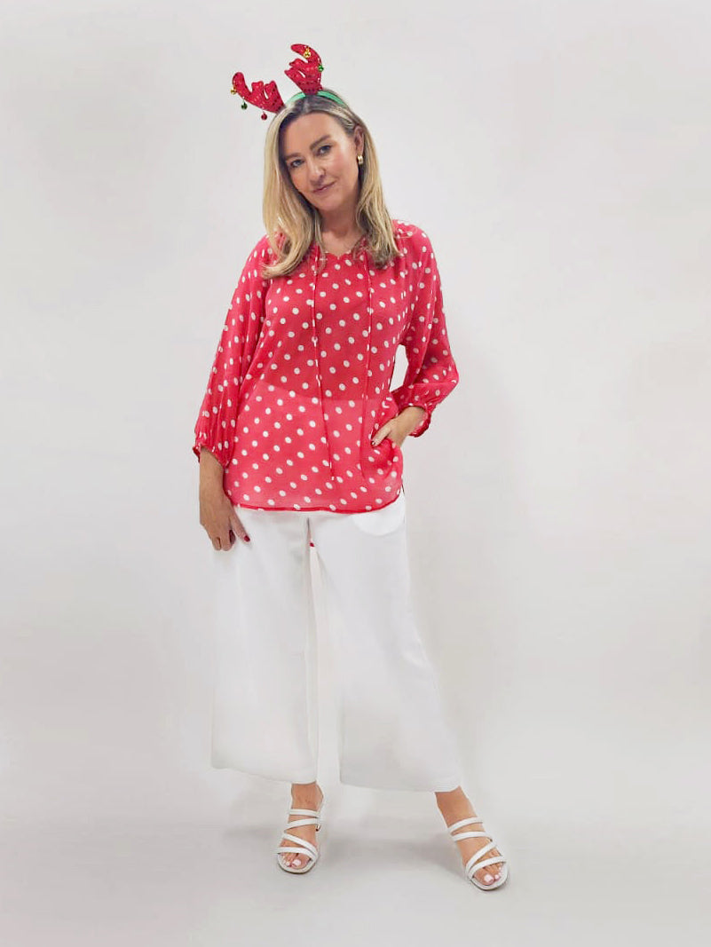 Person wearing a red polka dot blouse and white pants with reindeer antlers on a white background